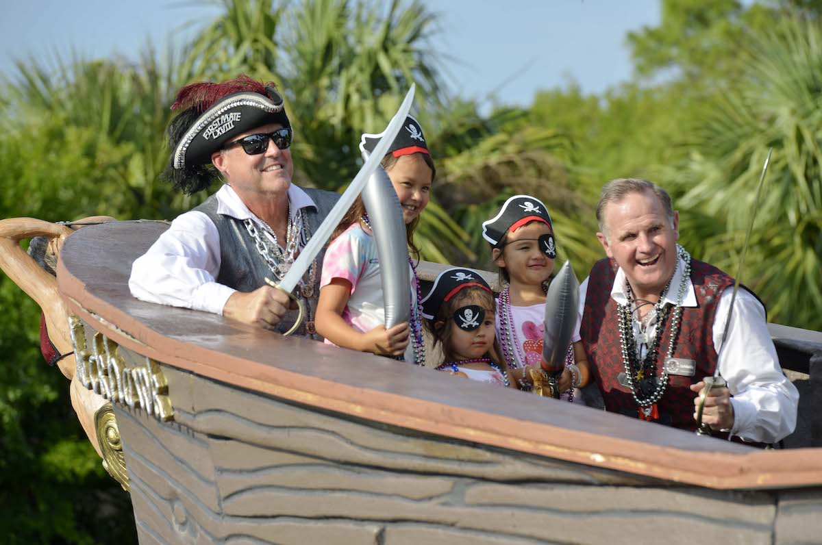 Two men dressed as pirates posing with three young girls wearing eye patches and pirate hats on a
pirate ship float